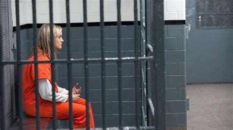 A Woman In An Orange Prison Outfit Sitting On A Bench