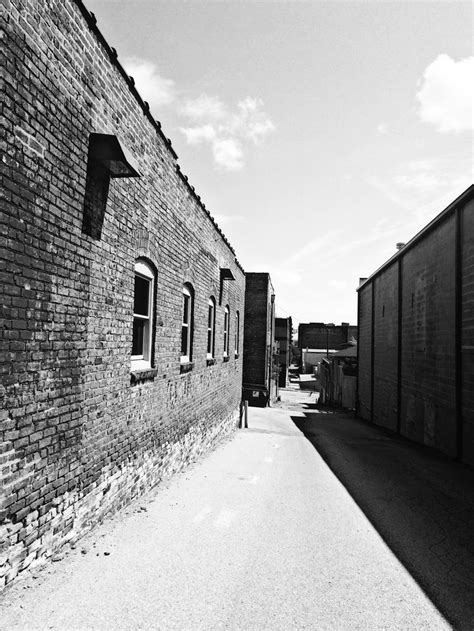 Black And White Photograph Of An Alley Way With Brick Buildings On Both