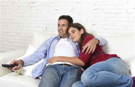 Couple In Love Cuddling On Home Couch Relaxing Watching Movie On Television With Man Holding