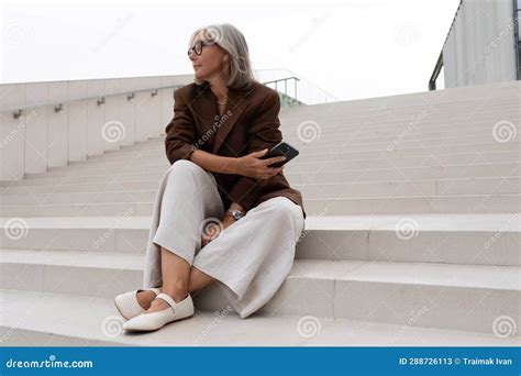 well groomed elderly gray haired business woman in a brown jacket and trousers sits on the steps