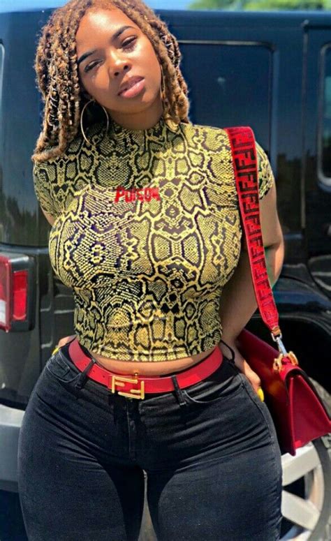 A Woman With Dreadlocks Standing In Front Of A Car Wearing A Snakeskin Top