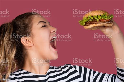 Hungry Cool Girl In Striped Tshirt Eating Hamburger Over Pink