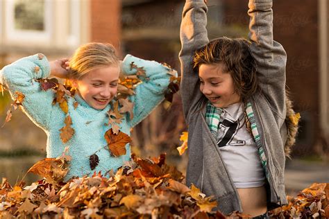 Girls Having Fun Playing In A Pile Of Autumn Leaves By Stocksy
