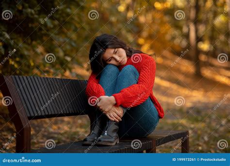 Depressed Young Woman Hugging Her Knees While Sitting On Bench At Yellow Autumn Park Stock Image