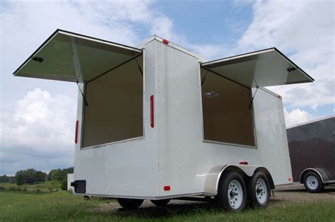 An Enclosed Trailer Parked In The Grass With Its Doors Open And Windows