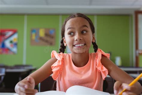 Portrait Of Smiling Mixed Race Schoolgirl Sitting At Desk In Classroom