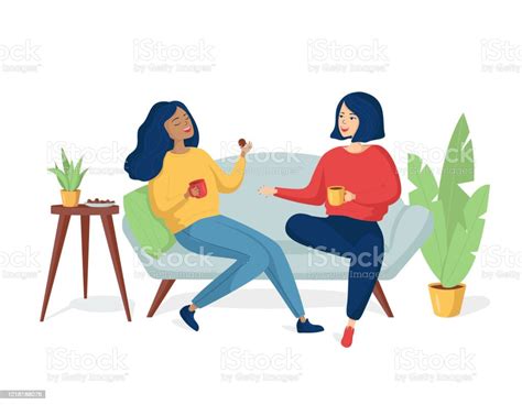 Two Young Happy Cheerful Women Are Sitting On The Couch And Laughing