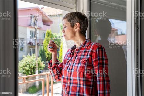 한 여성 성숙 또는 노인 여성 흡연 담배 밝은 날에 소방관과 함께 집에서 창문으로 담배를 피우는 실제 사람들은 매일 공간을 복사합니다 건강에 해로운 습관 니코틴 중독 45