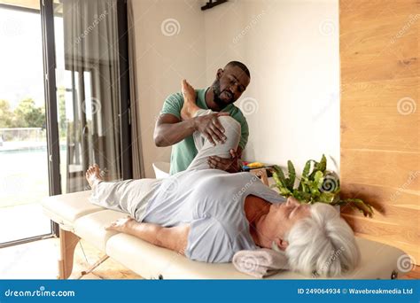 African American Male Physiotherapist Giving Leg Massage Therapy To Caucasian Senior Woman At