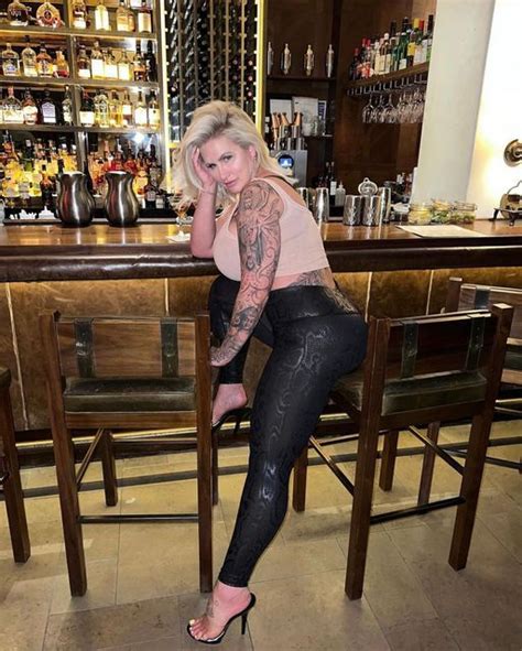 A Woman Sitting At A Bar With Tattoos On Her Arm And Leg Posing For