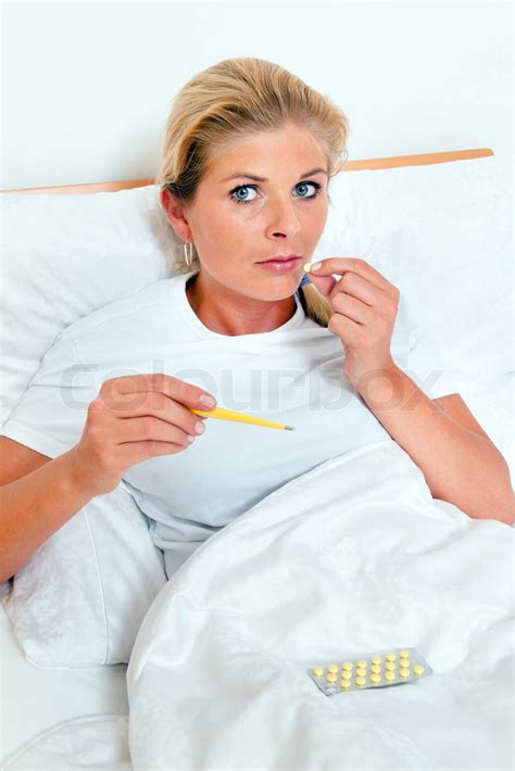 en kvinde er syg i sengen og har feber termometer stock foto colourbox