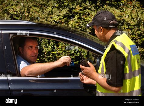 A Security Guard Checks An Identification Badge At The Gatehouse Of