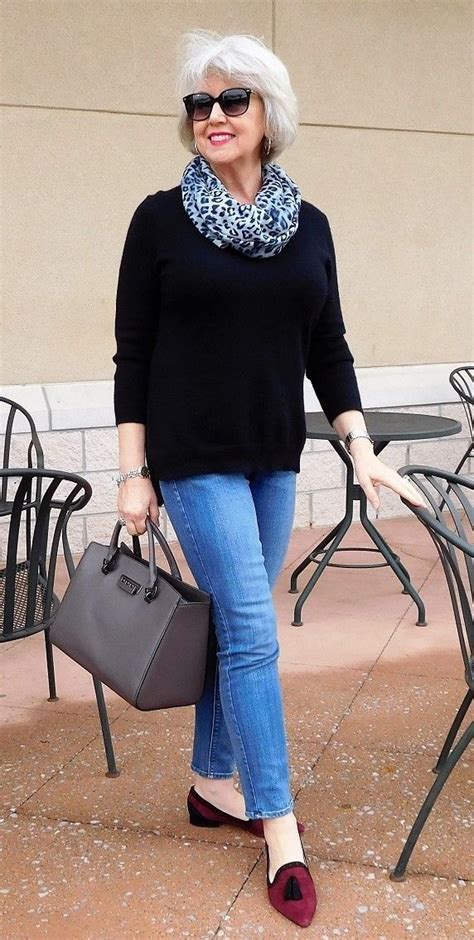 An Older Woman With White Hair Is Carrying A Gray Bag And Wearing Blue Jeans A Black Sweater