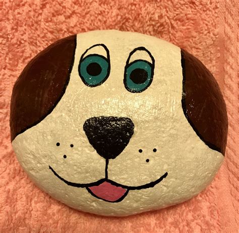 A Painted Rock With A Dogs Face And Blue Eyes On It Sitting On A Pink