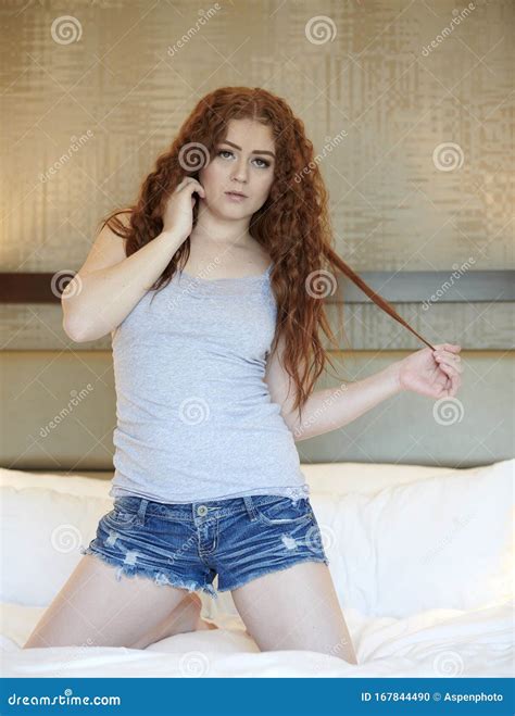 Redhead Woman Poses In Grey Tank Top And Denim Shorts Stock Photo