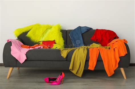 Messy Pile Of Colorful Clothes On Sofa And Shoes In Living Room Stock
