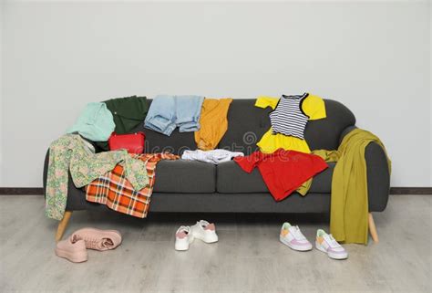 Messy Pile Of Clothes On Sofa And Shoes In Living Room Stock Photo