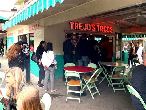 People Are Standing In Front Of A Taco Shop With Tables And Chairs On