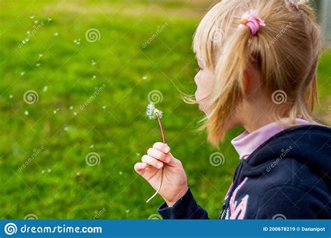 Close Up Of A Girl Blowing Dandelion Seeds Across A Fresh Green