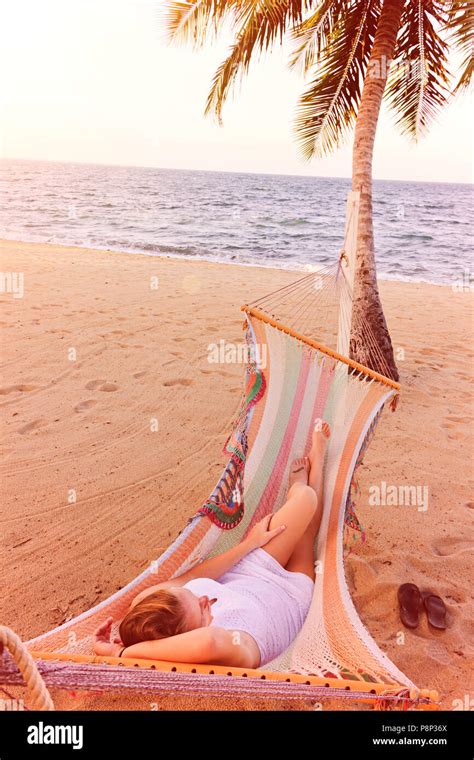Woman Relaxing In A Hammock On A Beach Next To A Palm Tree Stock Photo
