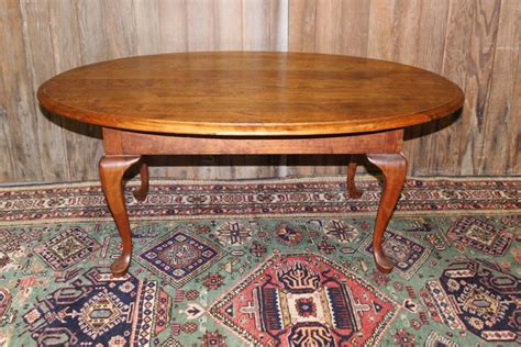 An oval carved trim coffee table made from cherry wood with lower display shelf and cabriole legs. Cherry Oval Coffee Table | Vintique Rental