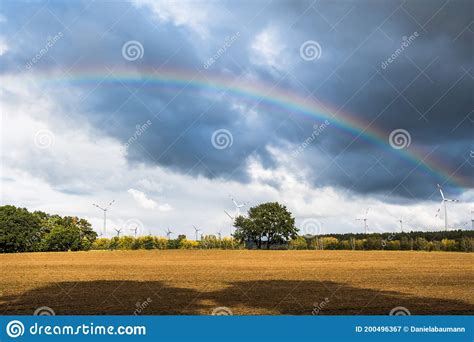 A Multicolored Rainbow Over A Field Of Wind Turbines And A Cloudy Sky