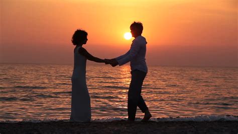 Young Man And Woman Are Spinning Around On The Beach At Sunset