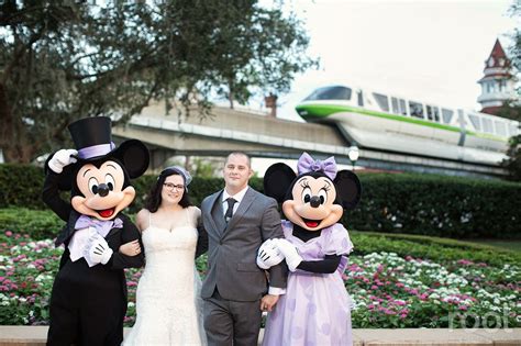 A Bride And Groom Pose For A Photo With Mickey Mouse In Front Of The