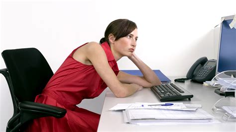 Young woman sitting at the desk and working on computer. Why your desk is hurting you and how to ease the pain ...