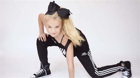 Jojo Siwa Is Wearing Black Dress And Bow On Head In White Background HD