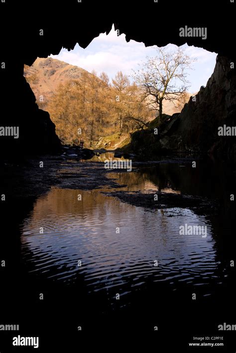 Silhouette Of Rydal Cave Entrance With Reflection Of Sunlit Lakeland