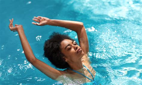 relaxed black girl floating in swimming pool with raised arms on hot summer day stock image