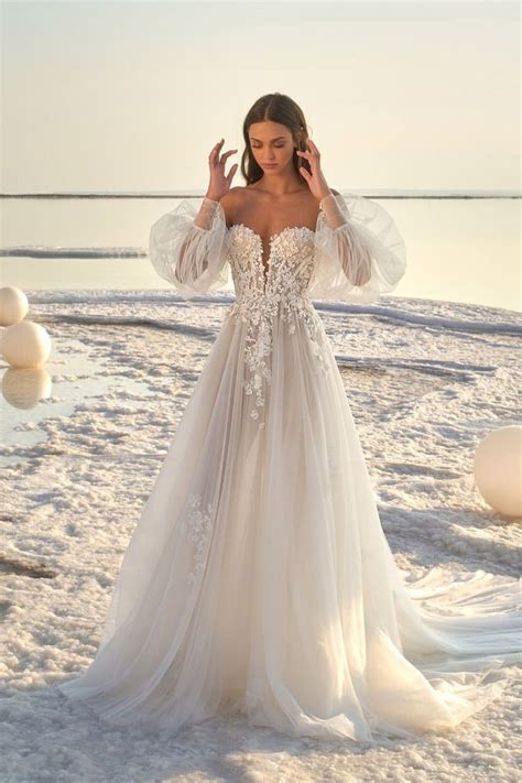 A Woman In A Wedding Dress Standing On The Beach With Her Hands Behind