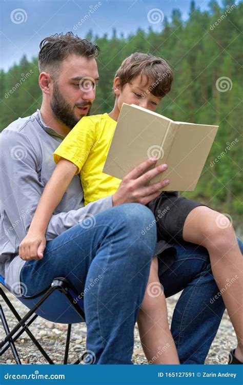 The Son Is Sitting On His Fathers Lap A Man Reads A Book To A Child