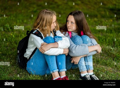 Two Girls Schoolgirl After School In Summer In The Park They Are Sitting On The Grass The