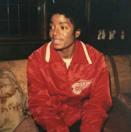 A Man Sitting On Top Of A Couch Wearing A Red Jacket