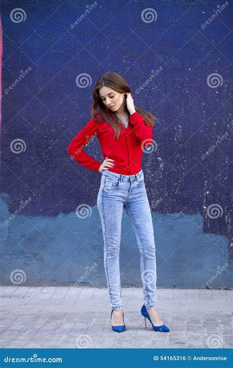 Young Beautiful Girl In Blue Jeans And A Red Shirt On The Background Of