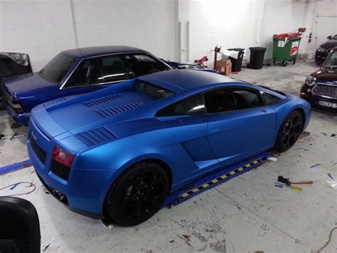 Two Blue Sports Cars Parked In A Garage Next To Each Other On A Flatbed