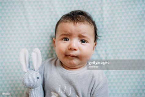 Portrait Of Baby Girl Lying On Bed With Toy Bunny Pulling Funny Face