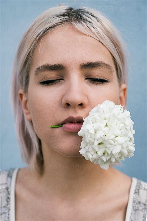 close up of blonde girl with bunch of white lilac in mouth by stocksy