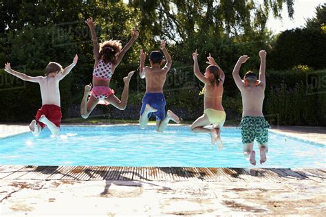 Rear View Of Children Jumping Into Outdoor Swimming Pool Stock Photo