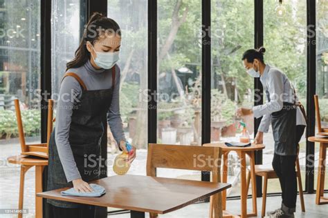 Asian Waitress Staff Wearing Protection Face Mask In Apron Cleaning Table With Disinfectant