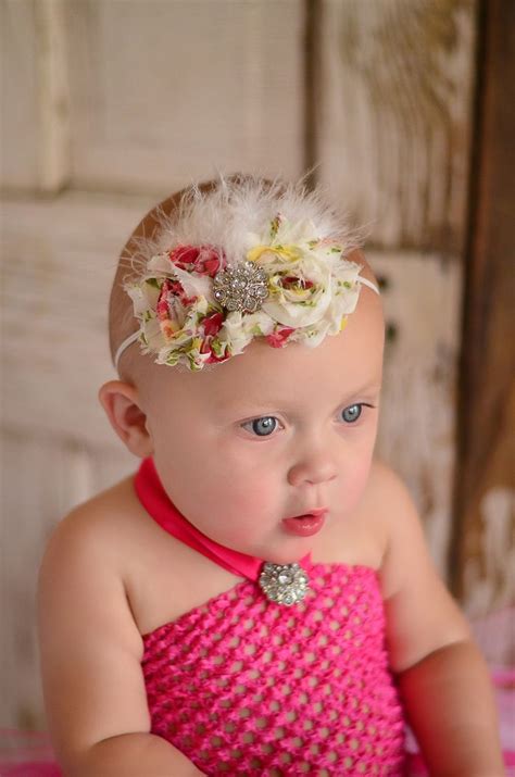 A Baby Girl Wearing A Pink Dress With Flowers And Feathers On Its Head