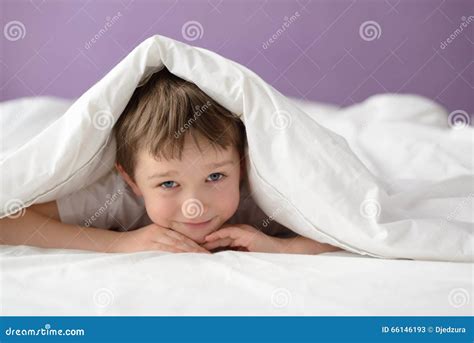 Happy Boy Hiding In Bed Under A White Blanket Or Coverlet Stock Image