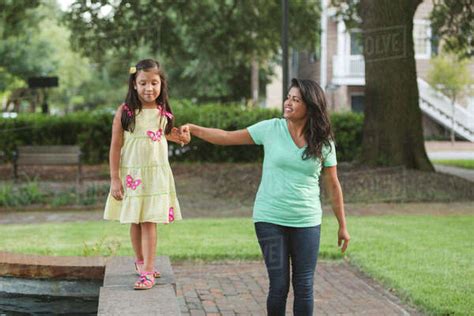 Hispanic Mother Holding Hand Of Daughter Walking On Park Wall Stock