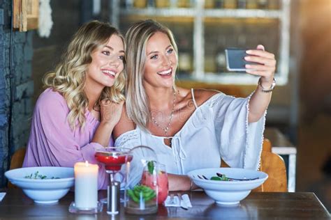 Two Girl Friends Eating Lunch In Restaurant And Using Smartphone Stock
