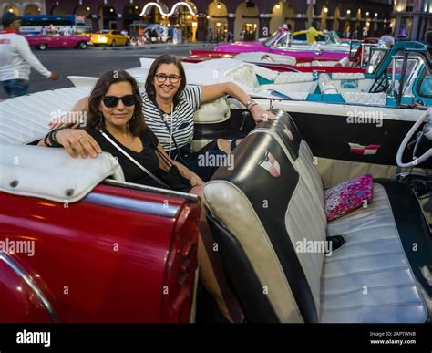 Two Women Sit In The Backseat Of A Vintage Car Looking At The Camera