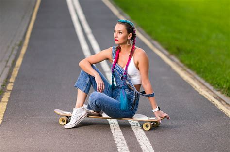 트렌디 한 세련된 스트리트 웨어를 입은 매력적인 백인 여성 롱 보드 스케이트 보드에서 레크리에이션 차가움을 즐기면서 도시의 스포츠 시간 동안 롱 보드에서 휴식을 취하십시오