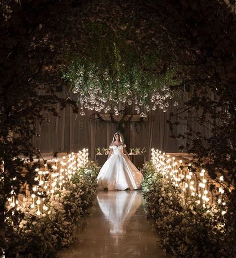 A Woman In A Wedding Dress Walking Down The Aisle With Candles Lit Up