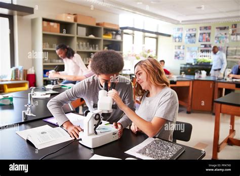 High School Students Looking Through Microscope In Biology Class Stock